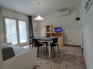 Ein kleiner Raum mit einem Bett, einem Tisch mit Stühlen, einem Fernseher und einem Fenster mit Vorhängen.