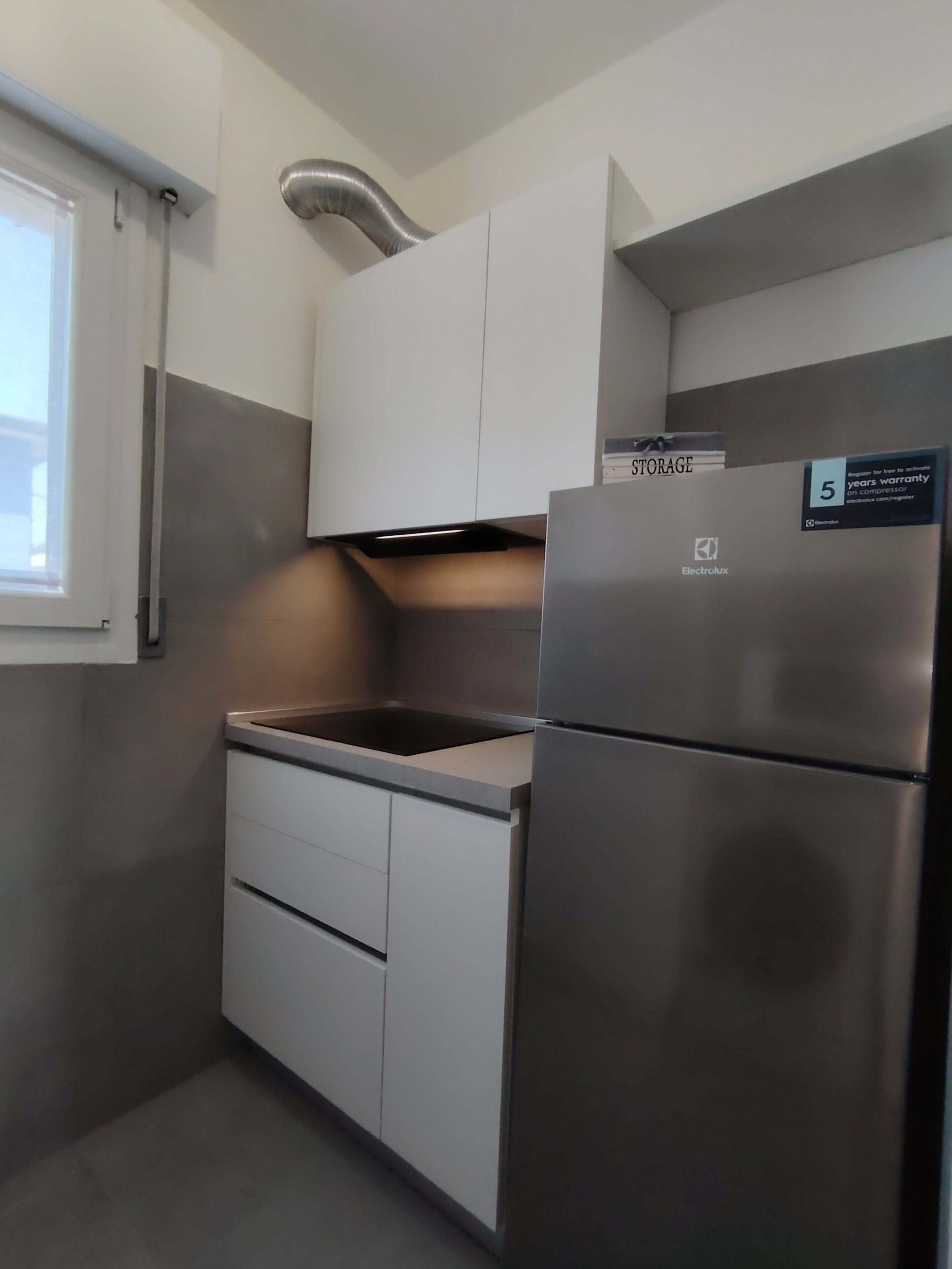 A compact kitchen with a stainless steel refrigerator, white cabinets, and a window.