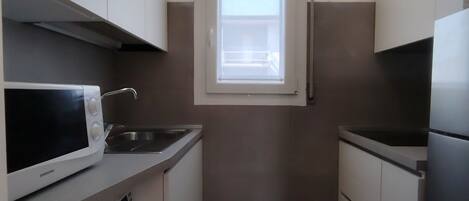 A compact kitchen with a washing machine, a microwave, a sink, and a window.