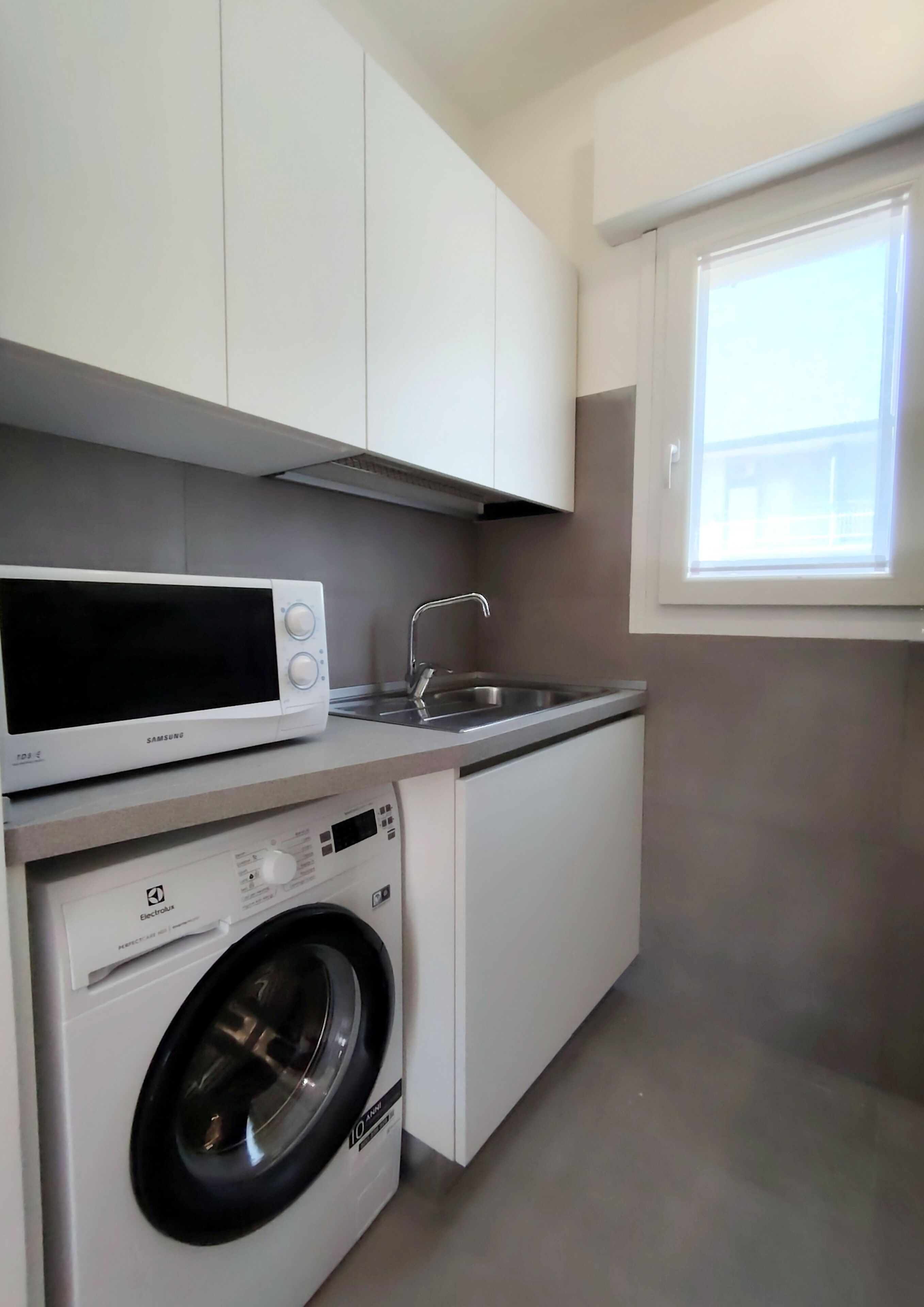A compact kitchen with a microwave, washing machine, and a window.