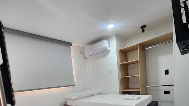 A modern bedroom with two beds, a built-in wardrobe, a small desk, and an air conditioning unit.