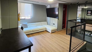 A room with a sofa, a TV, a table, and a staircase with a railing.