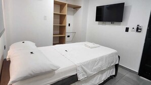 A single bed with white bedding, a mounted TV, and a built-in shelf unit.