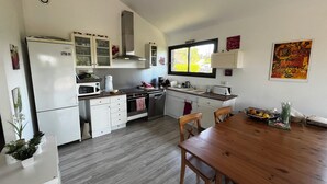 A modern kitchen with white cabinets, a wooden dining table, and a window providing natural light. - Modern house, 3 bedrooms, large quiet terrace, near Rocamadour, Dordogne... (Puybrun)