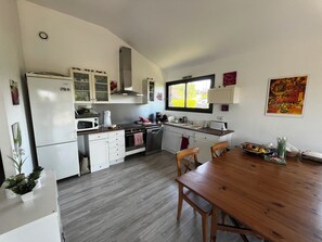 A modern kitchen with white cabinets, a wooden dining table, and a window providing natural light. - Modern house, 3 bedrooms, large quiet terrace, near Rocamadour, Dordogne... (Puybrun)
