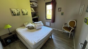 A bedroom with a bed, a chair, a window with curtains, a lamp, and wall art. - Modern house, 3 bedrooms, large quiet terrace, near Rocamadour, Dordogne... (Puybrun)