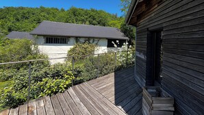 A wooden deck with a house in the background, surrounded by greenery. - Modern house, 3 bedrooms, large quiet terrace, near Rocamadour, Dordogne... (Puybrun)