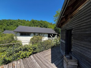 A wooden deck with a house in the background, surrounded by greenery. - Modern house, 3 bedrooms, large quiet terrace, near Rocamadour, Dordogne... (Puybrun)