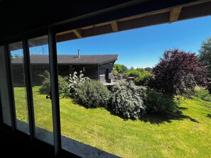A view through a window of a house with a well-maintained lawn, a patio with outdoor furniture, and a clear blue sky. - Modern house, 3 bedrooms, large quiet terrace, near Rocamadour, Dordogne... (Puybrun)