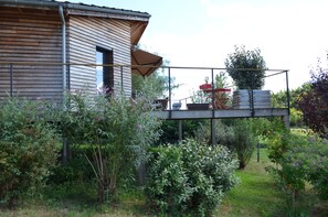 A wooden house with a balcony, surrounded by lush greenery and a garden. - Modern house, 3 bedrooms, large quiet terrace, near Rocamadour, Dordogne... (Puybrun)