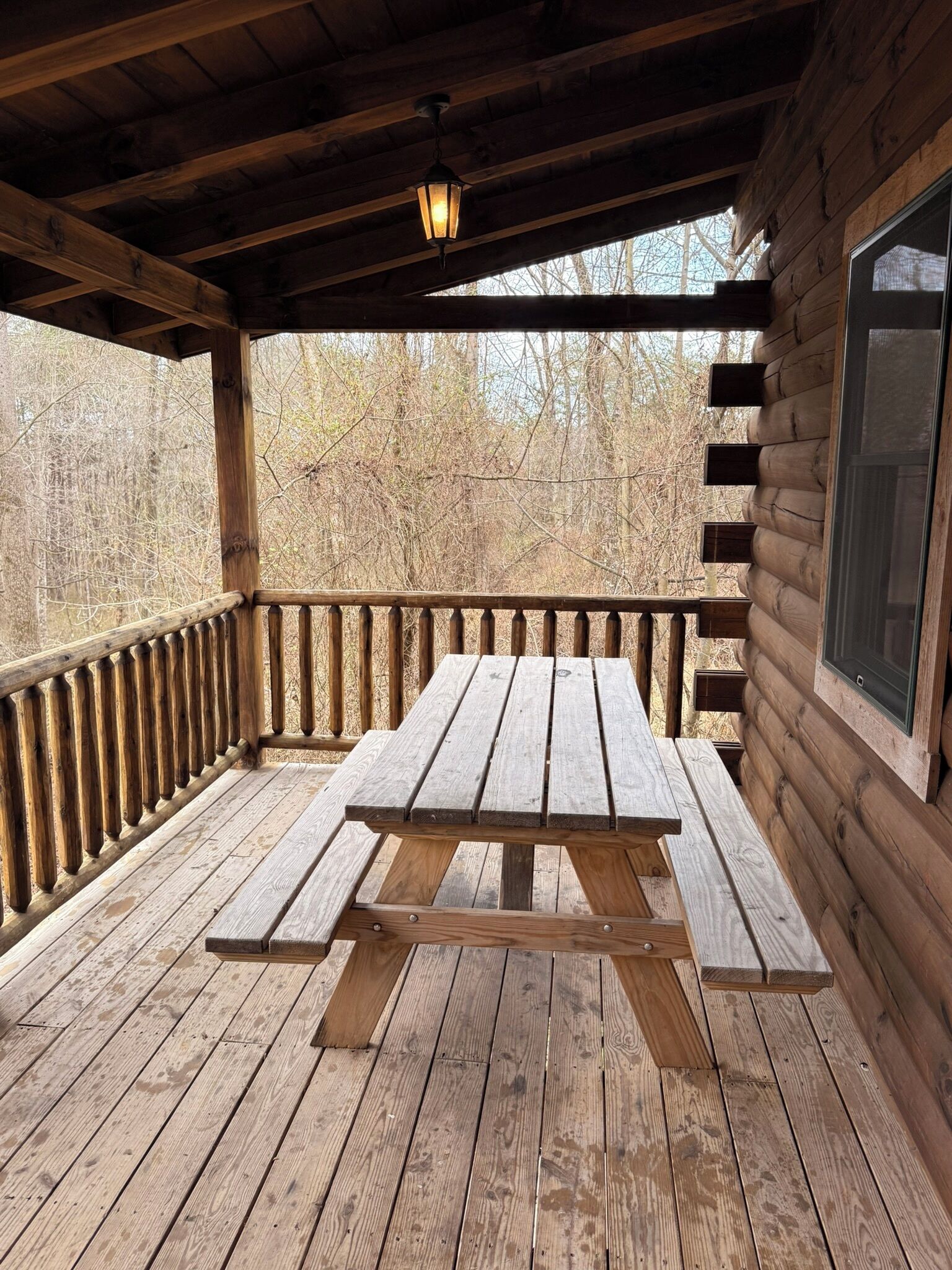 A wooden deck with a picnic table, wooden railings, and a window.