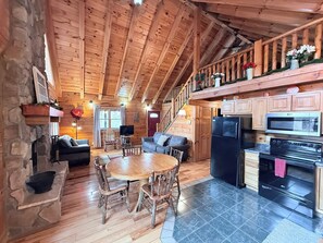 Interior de una cabaña de madera con comedor, cocina y una escalera que sube a un altillo.