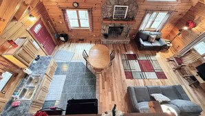 L’intérieur d’une cabane comprend une cheminée en pierre, des murs en bois, un coin repas et un espace salon confortable.