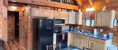A wooden cabin kitchen with a refrigerator, stove, microwave, and wooden cabinets.