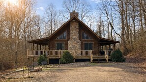 Une cabane en rondins avec une cheminée en pierre, une véranda avec des balustrades et un porche abrité.
