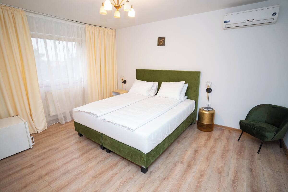Une chambre d’hôtel bien rangée, avec un lit, une chaise, une table de chevet et un appareil de climatisation.