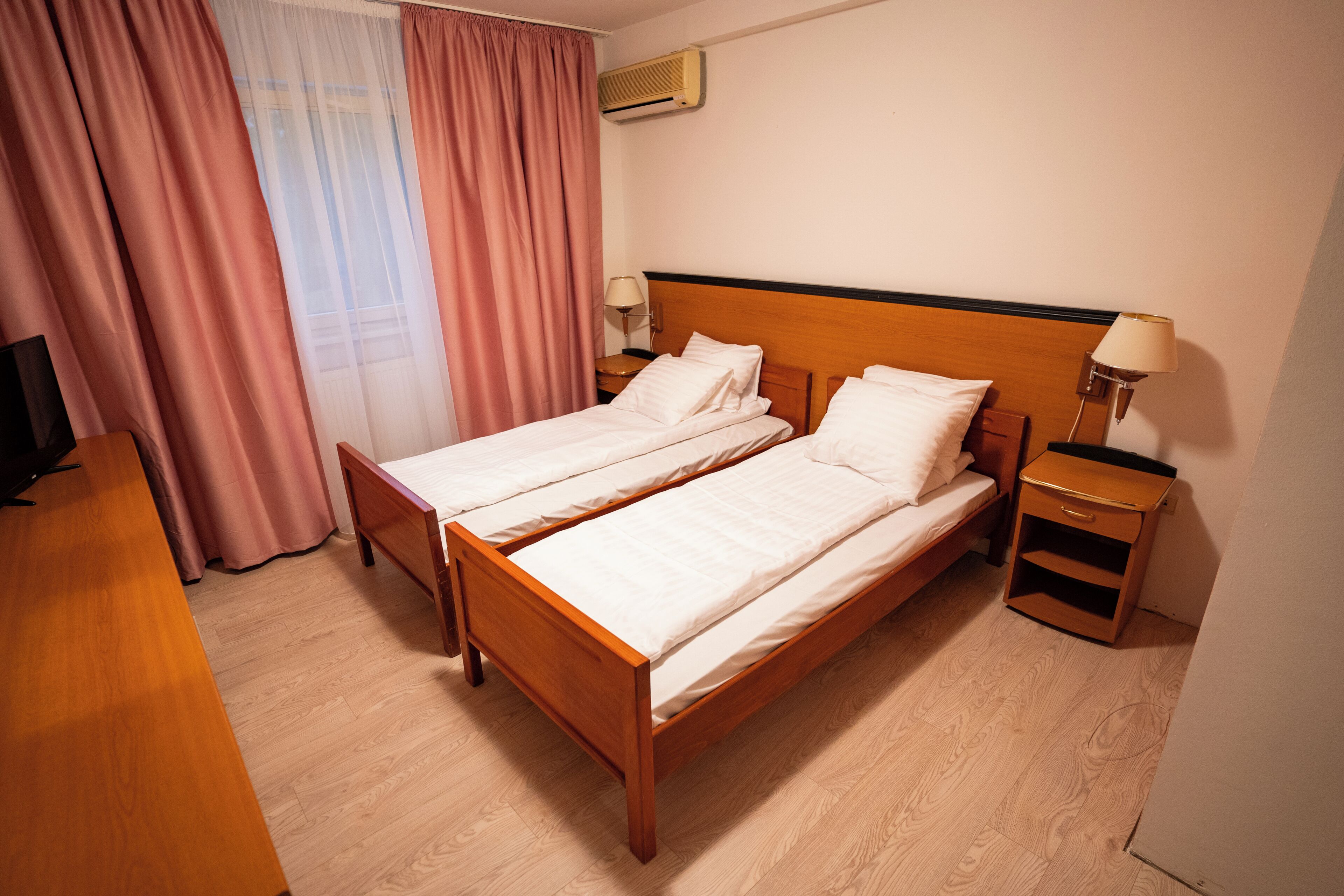 Una cama doble con cabecera de madera, una mesita de noche con lámpara y un televisor sobre un mueble bajo.
