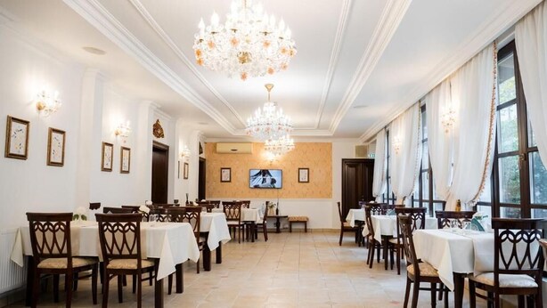 A dining area with tables, chairs, chandeliers, and a television screen. - Hotel Royal Plaza (Timișoara)