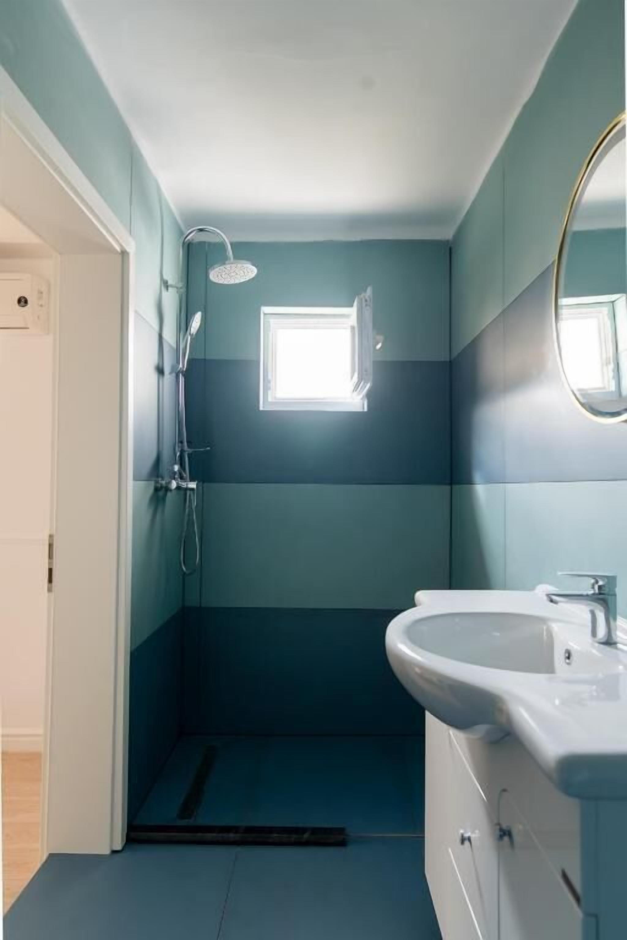 A bathroom with a shower, a sink, and a small window.