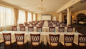 A conference room with multiple tables and chairs, a projector screen, and a chandelier. - Hotel Royal Plaza (Timișoara)