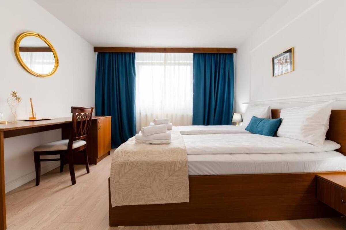 Une chambre d’hôtel avec un lit, un bureau, une chaise, un miroir et une fenêtre avec des rideaux.