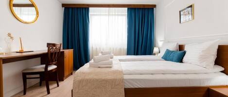 A hotel room with a bed, a desk, a chair, a mirror, and a window with curtains.
