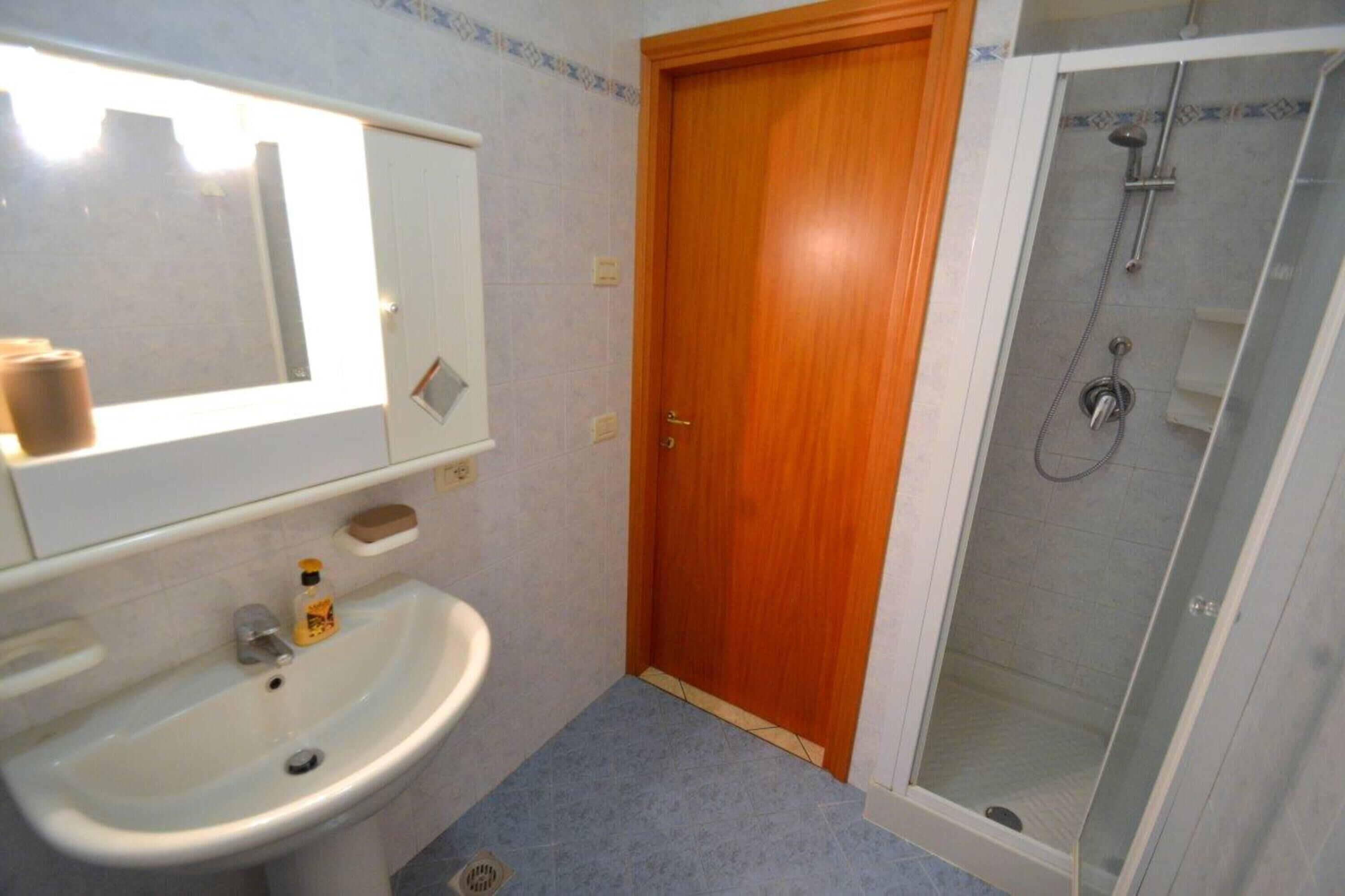 Une salle de bain avec un lavabo, un miroir, une porte en bois et une douche fermée par des parois en verre.