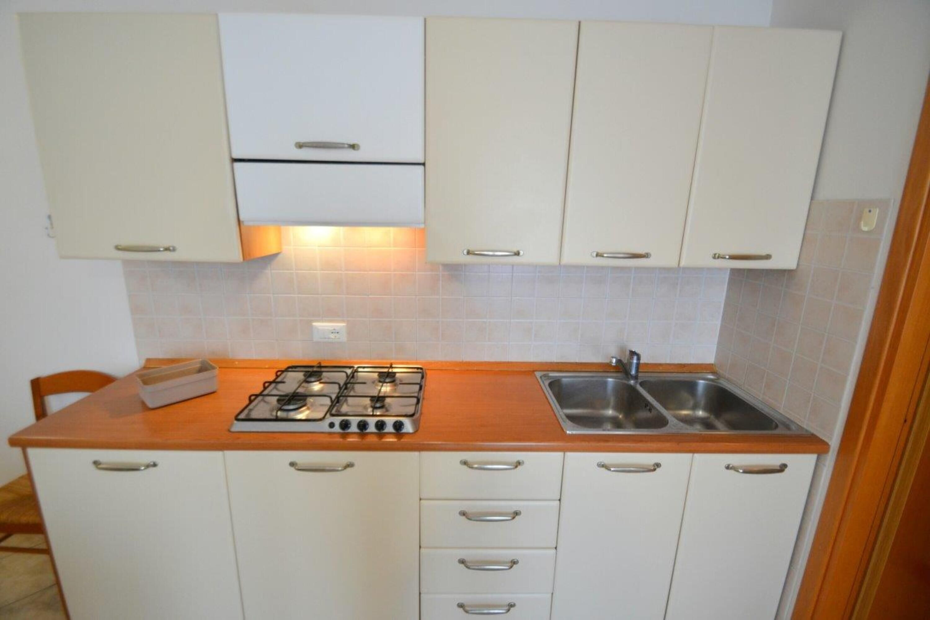 Een keuken met witte kastjes, een gasfornuis, een spoelbak en een houten aanrecht.