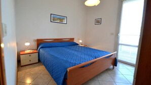 A bedroom with a bed, bedside tables, a window, and a door. - Cozy Holiday Escape With Relaxing Terrace (San Michele al Tagliamento)