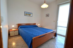 A bedroom with a bed, bedside tables, a window, and a door. - Cozy Holiday Escape With Relaxing Terrace (San Michele al Tagliamento)