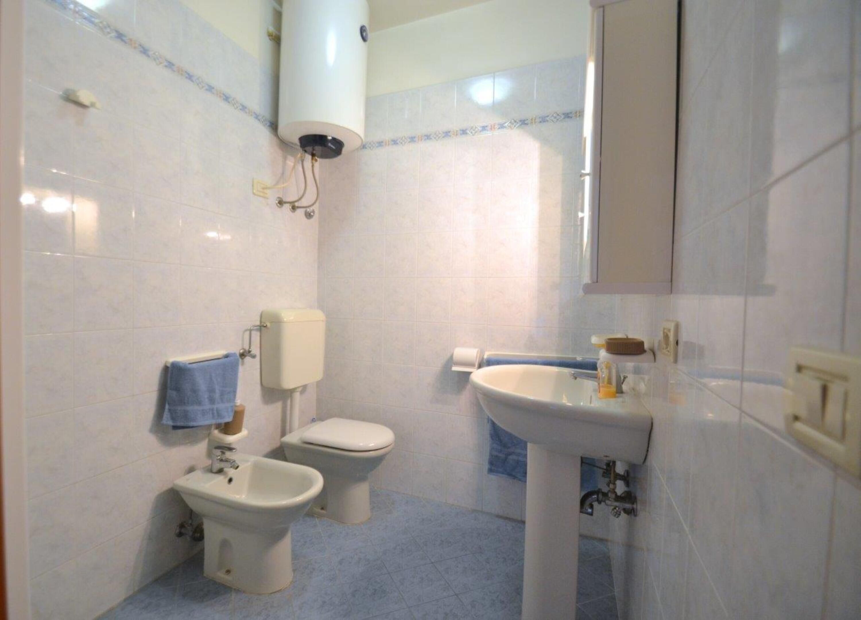 A bathroom with a toilet, bidet, sink, and a towel rack.