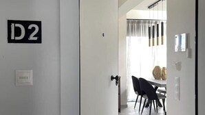 Ein modernes Interieur mit einer Tür mit der Aufschrift 'D2', einem Essbereich mit Tisch und Stühlen sowie einer Leuchte darüber.