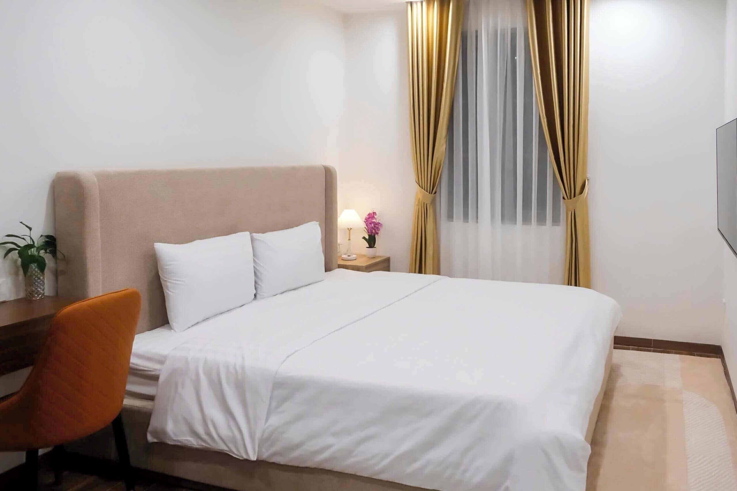 Ein Hotelzimmer mit Bett, Schreibtisch, Stuhl, Nachttisch mit Lampe und einem Fenster mit Vorhängen.