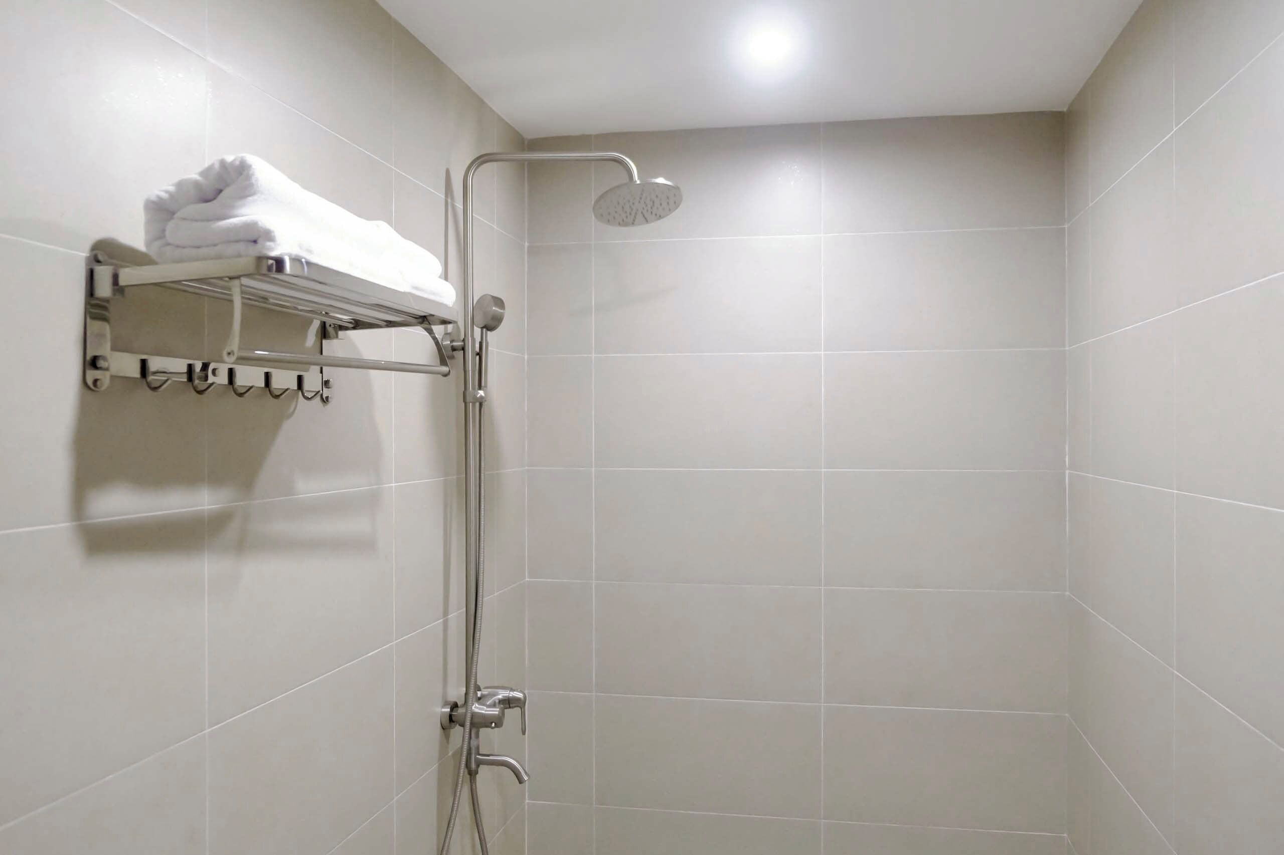 Eine Dusche mit Handbrause, ein Handtuchhalter mit gefalteten Handtüchern und ein Wandhandtuchhalter.