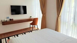 A hotel room with a bed, a TV mounted on the wall, a wooden console table, a chair, and sheer curtains. - KHEM BEACH HOTEL (An Thoi)