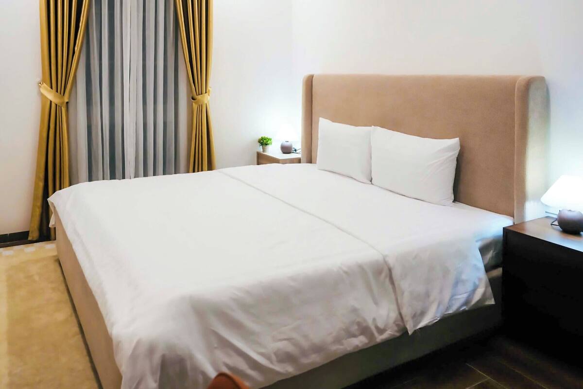 A neatly made bed with white bedding, a headboard, and a small bedside table with a lamp.