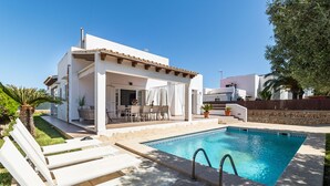 Zona junto a la piscina con un espacio de estar cubierto, una piscina y un edificio blanco con techo de tejas.