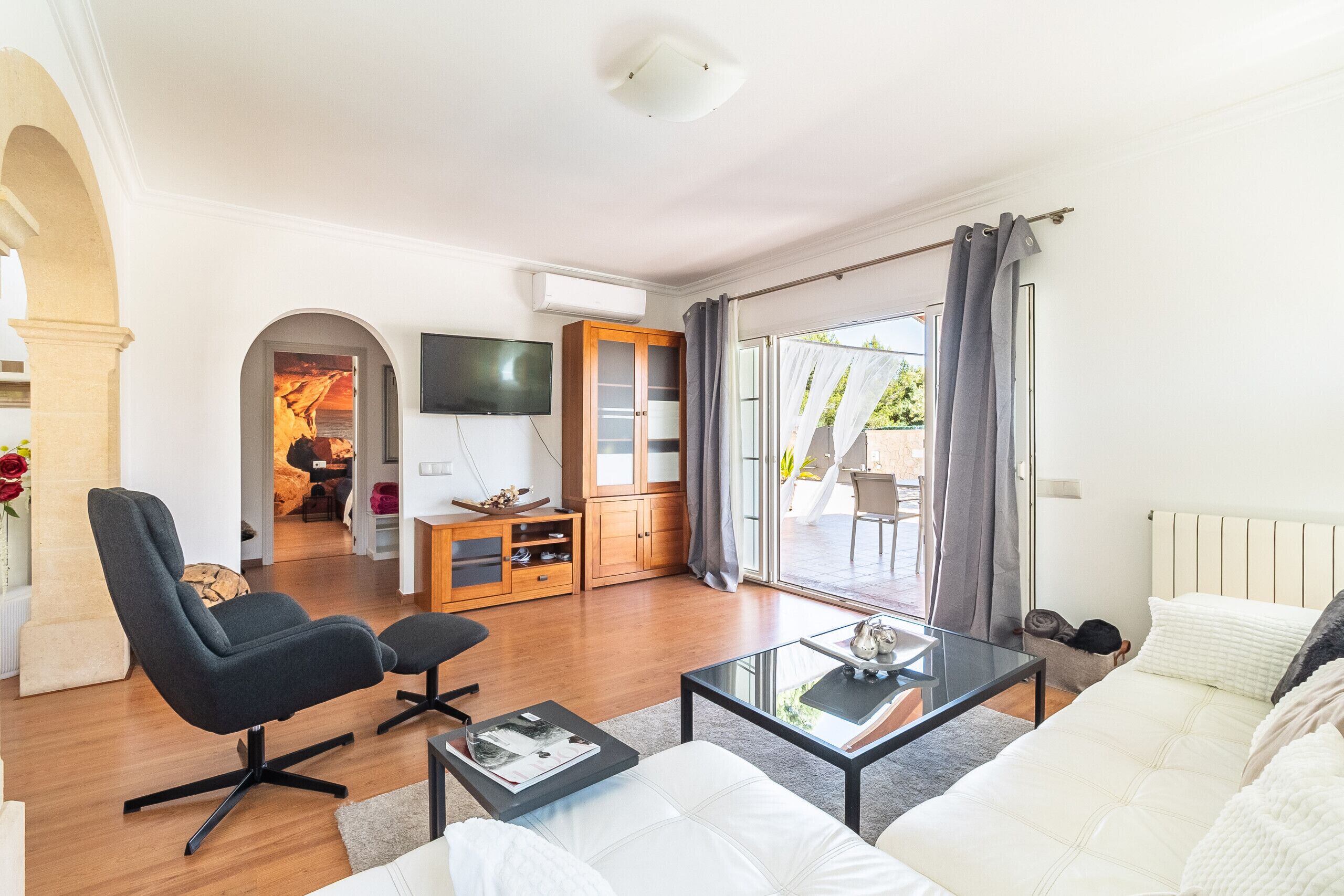 Een moderne woonkamer met een bank, fauteuil en salontafel, een televisie en een schuifdeur die leidt naar een buitenruimte.