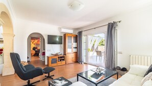 Una sala de estar moderna con sofá, sillón y mesa de centro, un televisor y un gran ventanal corredizo que da a un espacio exterior.