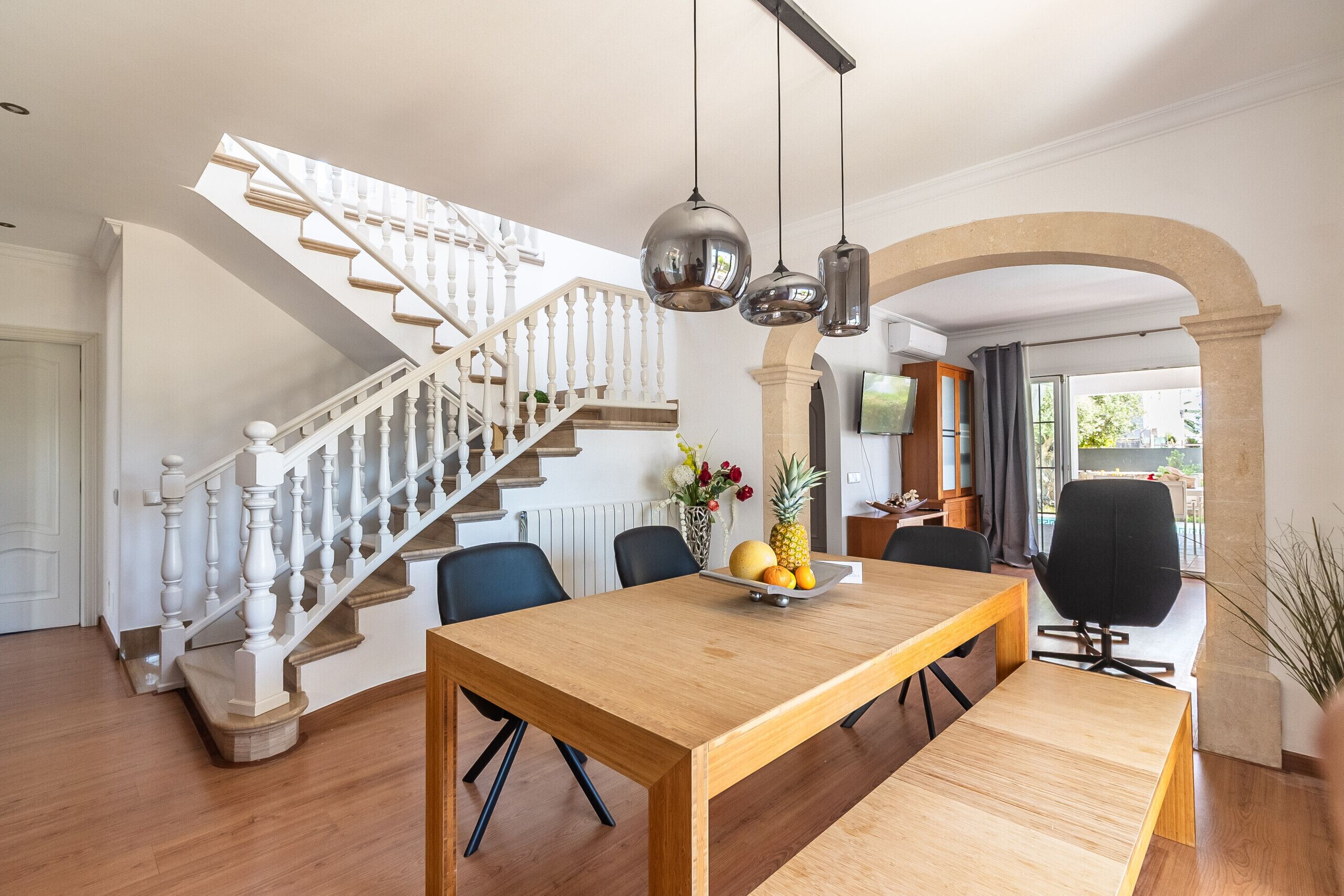 Een eetgedeelte met een houten tafel, stoelen, een fruitschaal en een trap met witte balustrades.