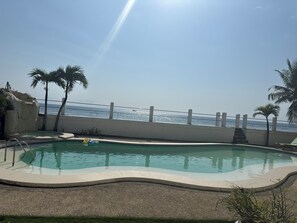 A swimming pool with a view of the ocean, surrounded by palm trees and a white fence. - A secluded stunning villa by the beach. (Carmen)