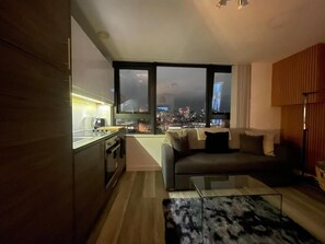 A modern living space with a kitchen, a sofa, a coffee table, and a large window with a city view. - Radio City Apartments near City Centre (Liverpool)