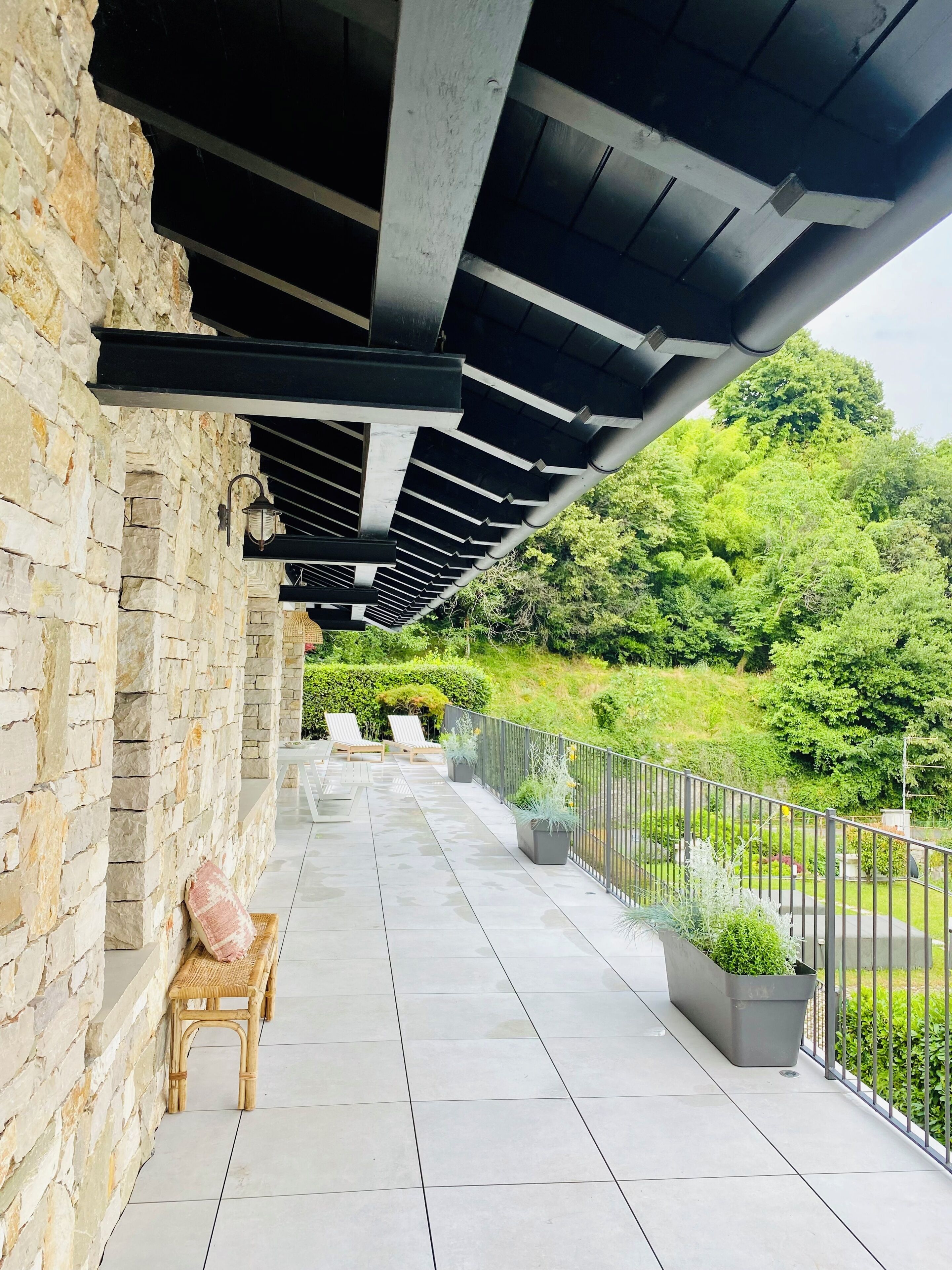 A covered outdoor area with stone walls, a pergola, and a view of a lush green landscape.
