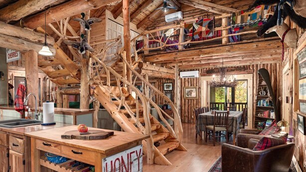 L’intérieur d’un chalet rustique comprend un escalier en bois, un coin cuisine, une table à manger et un espace salon confortable.