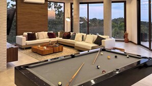 Un salon moderne doté d’une table de billard, de sièges confortables et de grandes fenêtres offrant une vue panoramique.