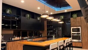Une cuisine moderne dotée d’un îlot central, de tabourets de bar, d’appareils électroménagers intégrés et de luminaires suspendus.