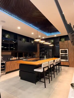 A modern kitchen with a central island, bar stools, built-in appliances, and pendant lighting. - Casa Vida Mar | Ocean View Villa (Playa Hermosa)