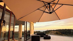 Un espace extérieur moderne, aménagé avec des sièges, un grand parasol, des murs en verre et une vue sur le paysage.