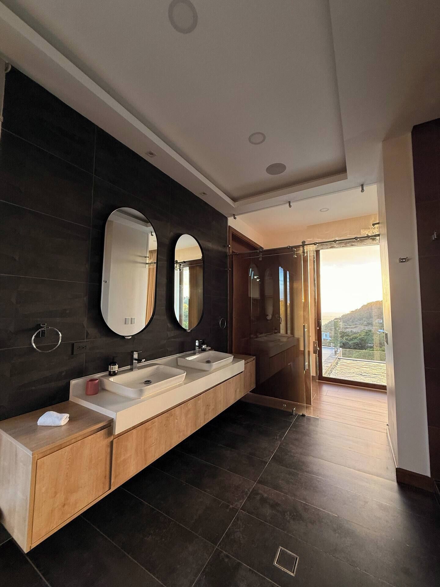 Un baño moderno con un tocador amplio, dos espejos y vistas a un balcón.