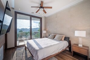 Ein Schlafzimmer mit Bett, Deckenventilator, Fernseher und Blick auf einen Balkon.